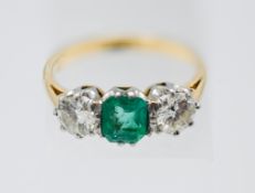 An emerald and diamond ring, centre trap cut emerald of good colour, two modern brilliant cut