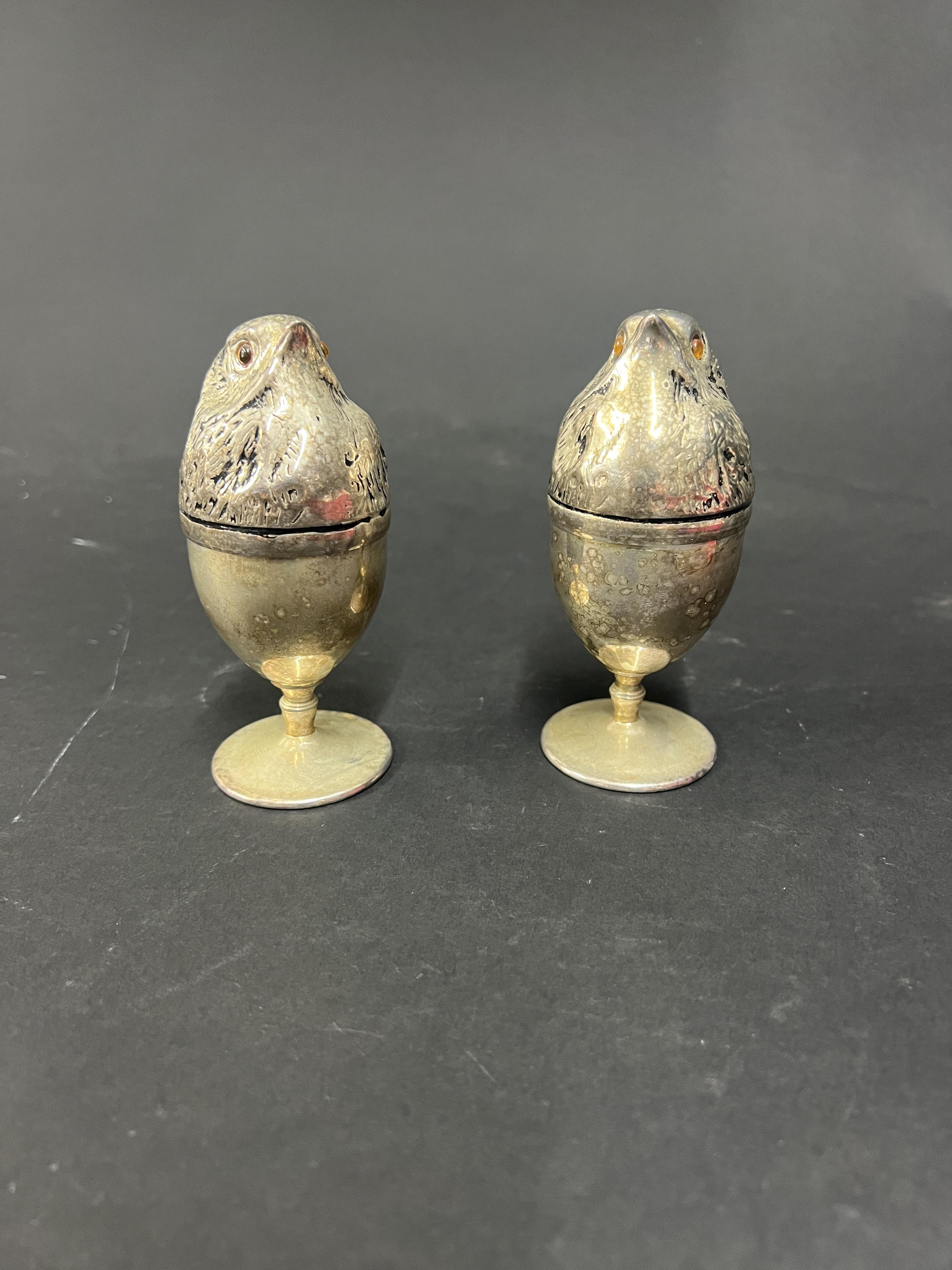 A pair of white metal novelty egg cups with bird head covers.