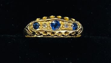 An 18ct yellow gold three stone sapphire and diamond ring, size M/N.