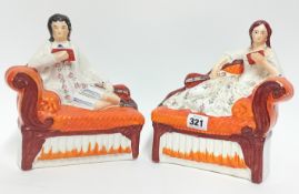 A pair of Staffordshire figures, depicting a man and woman reclining with books and lutes, in orange