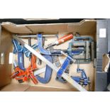 A collection of metal G clamps together with adjustable similar items, metal angle clamps, bench