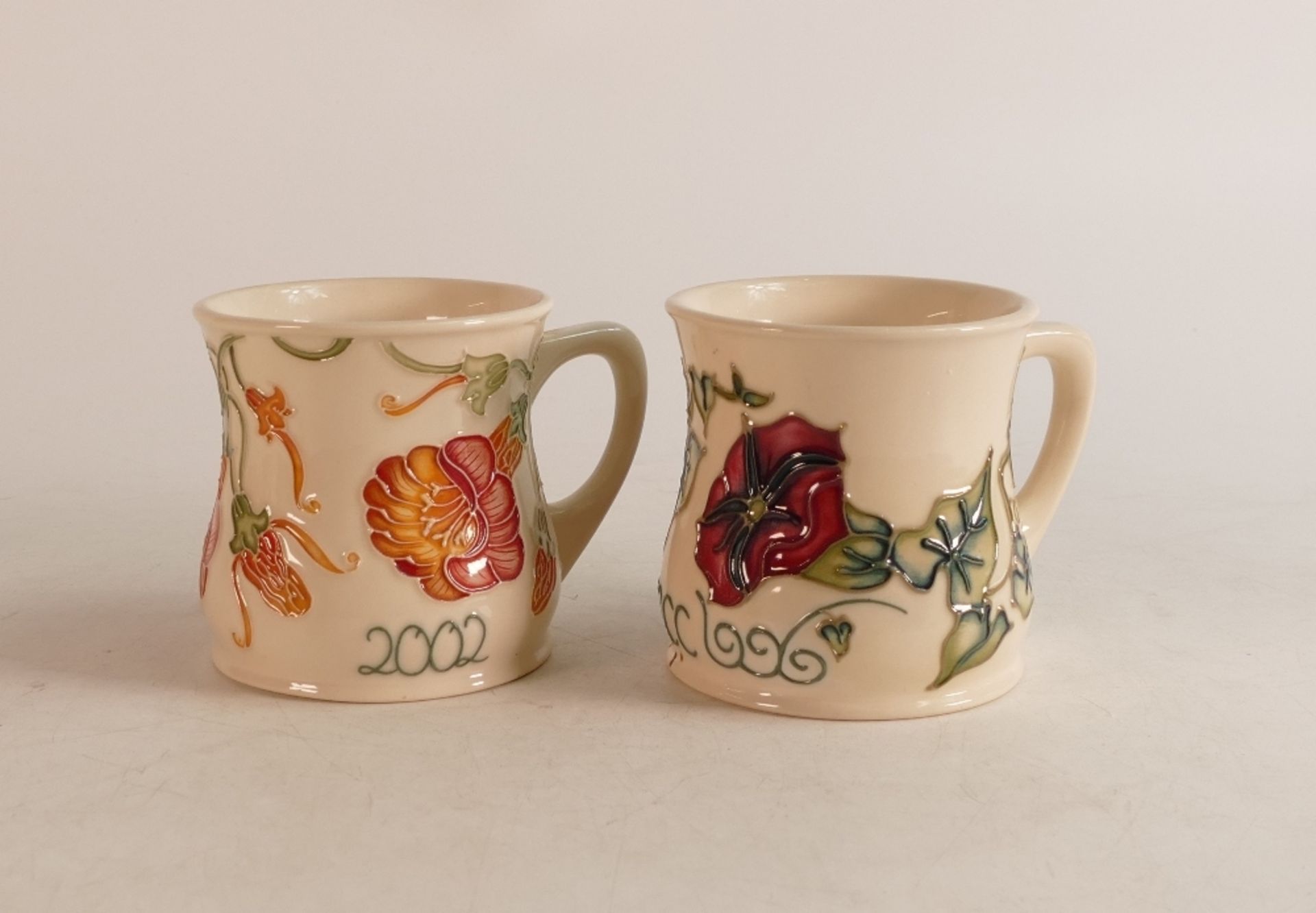 Two Moorcroft mugs to include 2002 year mug and MCC mug (2)