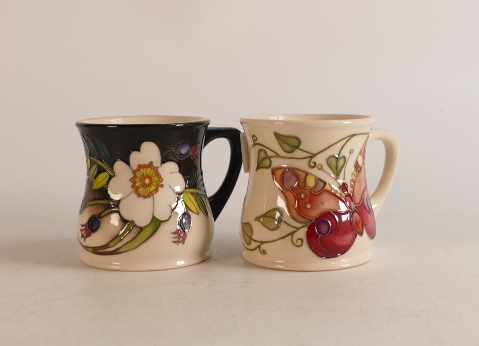 Two Moorcroft Mugs to include Butterfly and wild flowers on black/ white faded ground (red dot