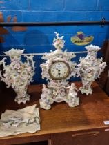 An early 20th Century clock garniture having floral encrusted decoration with cherubs and figures, p