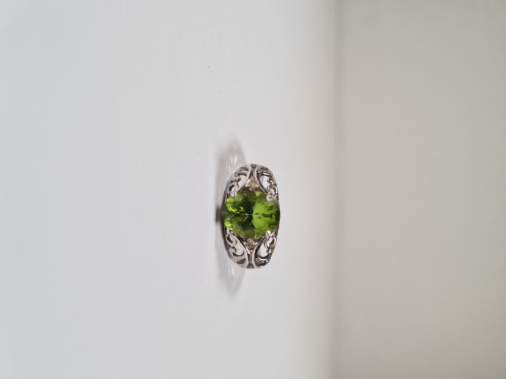 9ct white gold dress ring with oval mixed cut Peridot, each side set small diamond chips, on scrolli