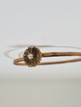 Unmarked yellow gold bangle with hook clasp below flowerhead, inset with seed pearls, 6cm diameter,