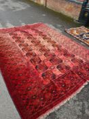 A large Afghan red ground rug having 3 rows of elephant pad medallions with geometric border (Some f