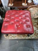A modern red leather Chesterfield armchair and a similar stool