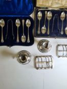 A cased set of decorative silver spoons and tongs, two silver toast racks by Hukin and Heath, a pair