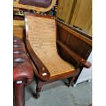 A mahogany steamer style chair having cane upholstery on turned front legs with folding leg rests