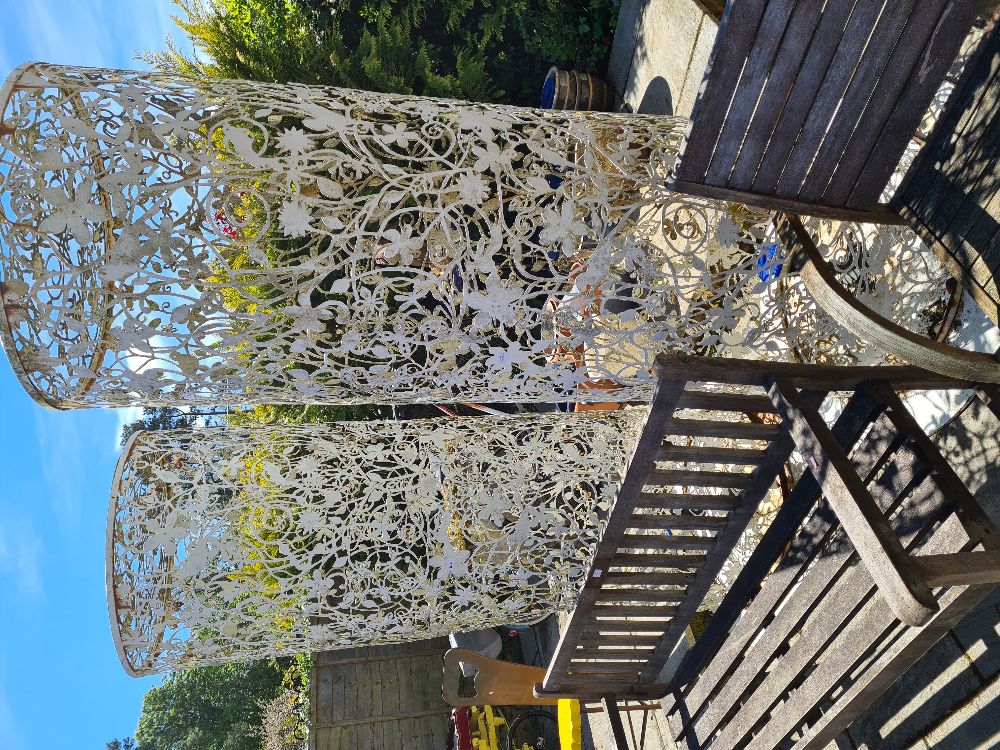 A pair of large pierced metal cylindrical columns containing lights, decorated birds and foliage