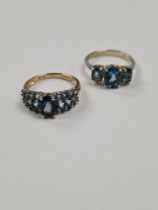Two contemporary 9ct gold dress ring set with blue topaz, one a trilogy the other cluster with centr