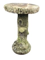 A composition stone garden birdbath cast in the form of a treetrunk, raised on tall naturalistic log