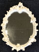 A painted oval rococo foliate scrolled mirror, the plaster leaf moulded frame formerly gilded. (19in