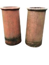 A pair of terracotta chimney pots with rounded moulded tops above tapering cylindrical bodies. (23.