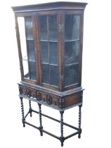 An Edwardian C17th style oak display cabinet on stand, the cornice above a pair of glazed doors with