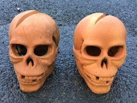 A pair of terracotta garden ornaments modelled as skeleton skulls with head wounds. (9in x 10in x