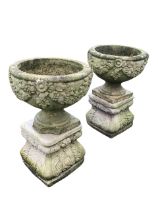 A pair of composition stone garden urns on stands, cast with vine swags and leaves, supported on