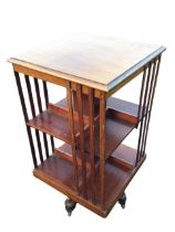 An Edwardian mahogany revolving bookcase, the moulded square top above two open shelves framed by