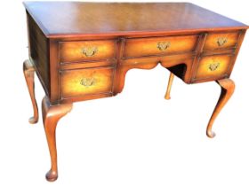A rectangular walnut desk, with moulded top above a shaped kneehole and frieze drawer, framed by