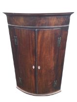 A Georgian mahogany bowfronted corner cupboard, the moulded cornice above a plain frieze and a