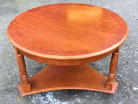 A circular crossbanded teak coffee table raised on paired column legs joined by a concave triangular