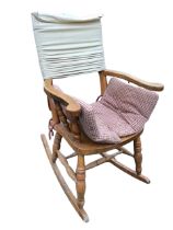 A beech rocking chair, lacking back and with added cushions, the scrolled arms on spindles above a