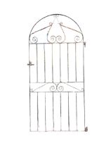 An arched wrought iron garden gate with scrolled decoration and tubular spindles to rectangular