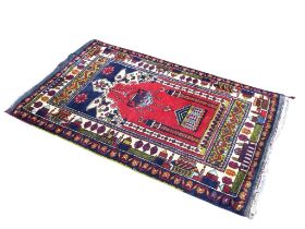 An Afghan wool prayer rug, the red ground Mihrab with hanging lantern and mosque, within elaborate