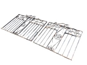 A pair of wrought iron garden gates, with scrolled crests above scrolled and spindled panels,