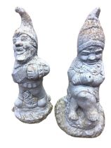A pair of composition stone garden gnomes, one playing an accordion, the other seated fishing,