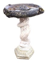 A composition stone birdbath, the circular bowl cast with shells, supported on a dolphin column with