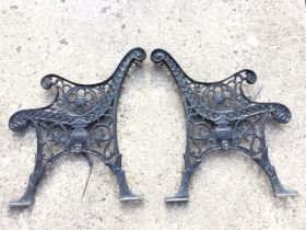 A pair of cast iron bench ends with scrolled arms above pierced roundels with lionheads, raised on