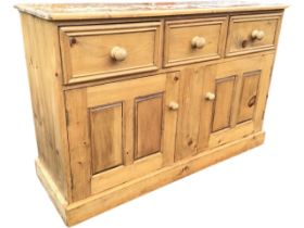 A Victorian style pine dresser base, the rectangular top above three panelled knobbed drawers and