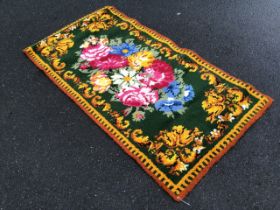 A handmade 60s latch hook wool rug with green field sewn with bright floral spray, within