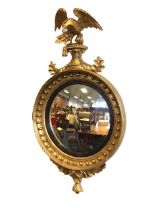 A regency giltwood circular convex wall mirror, the scrolling foliate crest with eagle finial