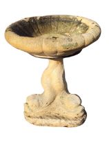 A composition stone birdbath with circular ribbed bowl on dolphin tail support, above a triangular
