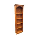 A pine open bookcase, the moulded cornice above an arched apron and five shelves, raised on a