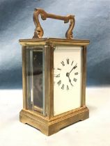 A brass carriage clock with shaped handle above a rectangular bevelled glazed top and channelled