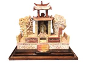 An Edwardian carved soapstone temple, with kneeling figure in covered building framed by stylised