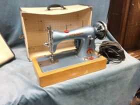 A 50s cased Atlas portable electric sewing machine, with bakelite foot pedal on a beech base, the