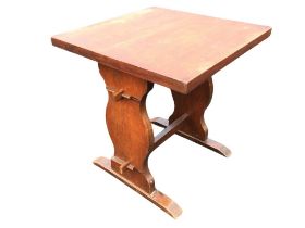 An oak table, the square top raised on shaped trestle supports joined by pegged stretchers, on