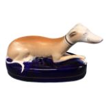 A Staffordshire ceramic inkwell in the form of a recumbent greyhound on an elliptical blue glazed