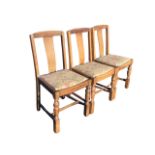 A set of three 30s oak dining chairs with carved crestrails and solid splats above drop-in