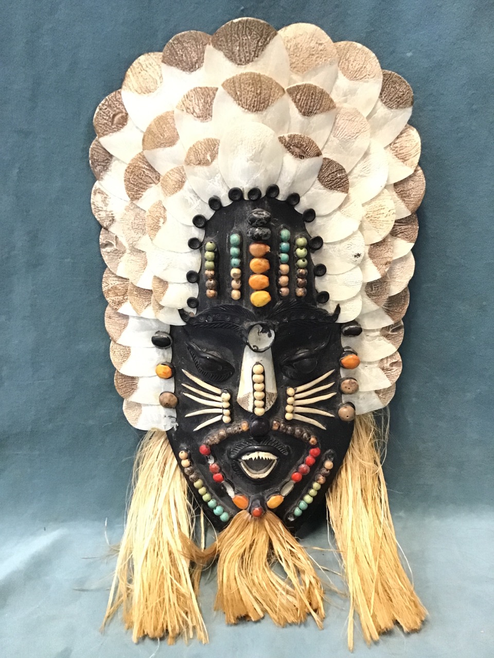 An Amazonian Indian hardwood wall mask decorated with coloured beads and seeds, scales, piranha