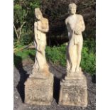 A pair of classical composition stone garden statues with a draped couple standing by logs on square