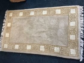 A Chinese wool rug with an ecru field within greek key and panel borders. (59.5in x 36in)