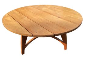 A contemporary circular hardwood dining table with plank top in a tripod base with curved tapering