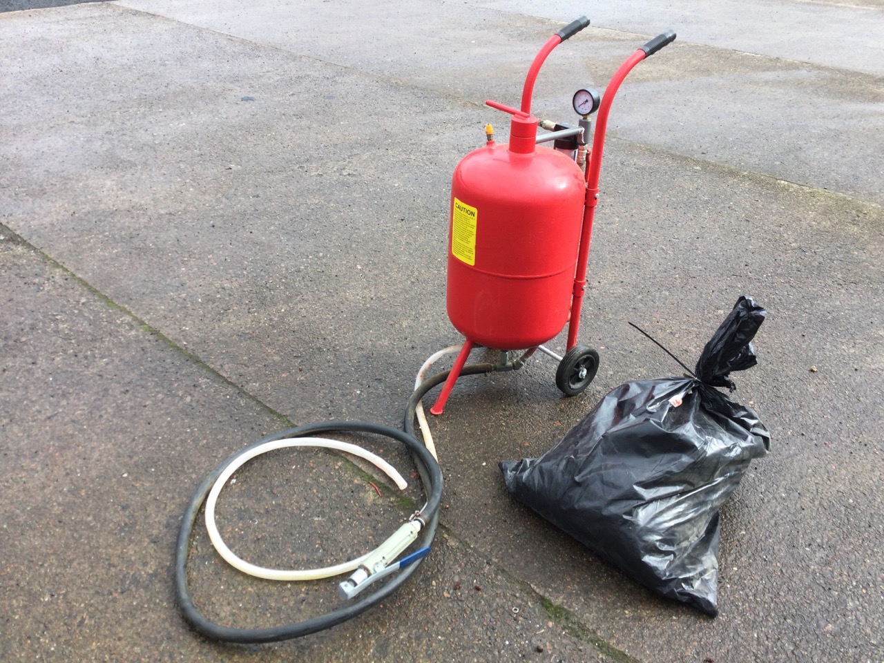A 10 gallon pressurised sandblasting machine on trolley stand, complete with a bag of soda