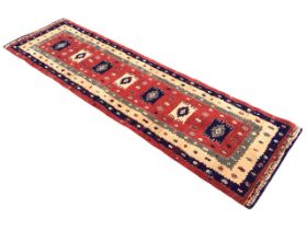 A Turkish style wool runner by Kayam with square medallions on russet ground, within multiple